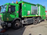 a green garbage truck that is parked in a lot