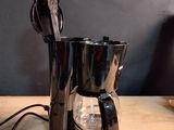 une cafetière noire posée sur une table en bois, à côté d'une tasse