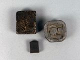 deux morceaux de métal et un objet métallique carré posés sur une surface blanche