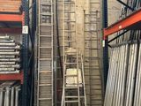 Plusieurs échelles sont empilées dans un entrepôt, et une échelle est appuyée contre le mur.