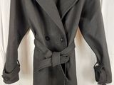 a grey coat is hanging on a hanger in front of a white curtain
