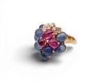 un gros plan d'une bague en or sertie de pierres bleues, roses et blanches