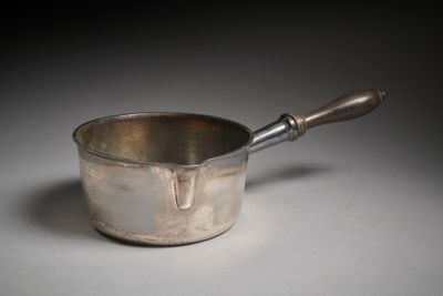 une casserole en argent avec un manche en bois posée sur une table