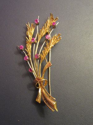 an image of a gold brooch with pink stones on a black surface
