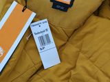 a jacket with a tag on it sitting on top of a pile of clothes