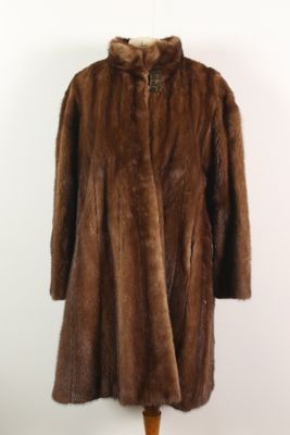un manteau de fourrure marron posé sur un mannequin, devant un mur blanc