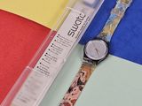 une montre posée sur une surface colorée, à côté d'un stylo