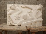 a white sculpture on a wooden bench in front of a brick wall