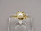 bague en or ornée d'une perle et de diamants, posée sur une plaque transparente