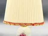 une lampe blanche ornée d'une rose rose, à côté d'un abat-jour