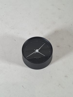 une petite horloge noire posée sur une table blanche