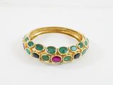 un gros plan d'une bague en or sertie de pierres vertes, roses et bleues