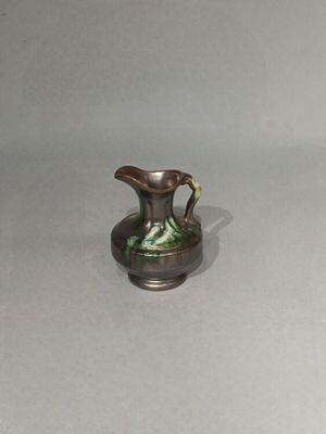un petit vase vert et blanc posé sur une surface blanche