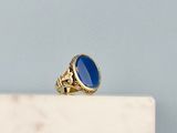 une image représentant une bague en or sertie d'une pierre bleue, posée sur un bloc de marbre