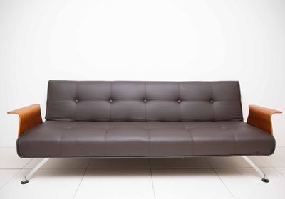 canapé-futon en cuir marron adossé à un mur blanc, avec un accoudoir en bois