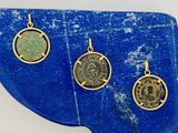trois pendentifs représentant des pièces de monnaie romaines antiques posés sur une dalle de pierre bleue