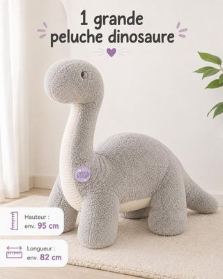 Le grand dinosaure en peluche est assis sur le tapis, à côté d'une plante en pot.