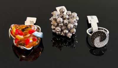 Trois bagues différentes sont posées sur une table devant un fond noir.