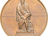 médaille de bronze représentant un homme assis sur une chaise, un livre sur les genoux