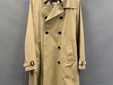 un trench-coat beige suspendu à un cintre devant un mur gris