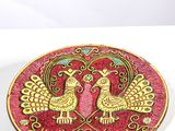 assiette rouge et dorée ornée de deux oiseaux sur un fond blanc