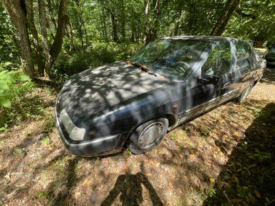 une voiture abandonnée dans la boue, au milieu des bois
