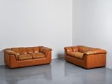 two brown leather couches in a white room with a white wall