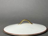 a white and gold plate with a wooden handle on a gray surface