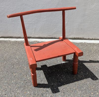 une chaise rouge posée sur le trottoir devant un mur blanc