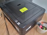 une imprimante posée sur un bureau, sur laquelle est collé un autocollant jaune
