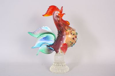 une figurine en verre représentant un coq, posée sur un socle transparent