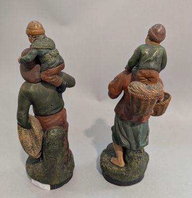 deux figurines représentant des personnes portant des paniers, posées sur une surface blanche
