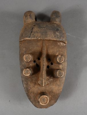 an old wooden mask hanging on a wall on a gray surface