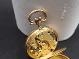 a gold pocket watch sitting on a table next to a white vase