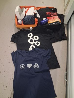 trois t-shirts par terre, à côté d'une valise ouverte