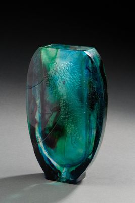 un vase en verre vert et bleu posé sur une surface blanche