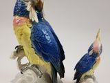 two figurines of parrots sitting on top of a tree branch