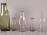 trois bouteilles vides et deux vases en verre vides posés sur une table