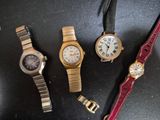 trois montres sont posées sur une surface noire, à côté d'un bracelet rouge