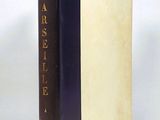 an old book with a black cover sitting on top of a white table