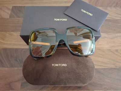 Lunettes de soleil Tommy Ford avec leur boîte et leur étui, posées sur un parquet
