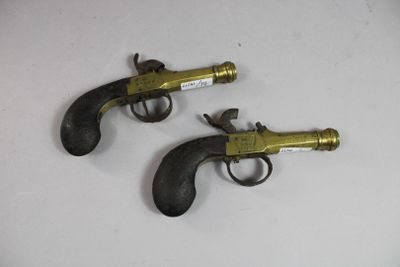 deux revolvers anciens en laiton posés sur une surface blanche