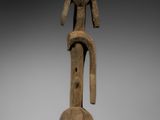 une statue en bois représentant un homme au long cou et aux longues jambes