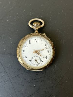 une petite montre de poche en or posée sur une surface noire