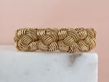 a close up of a gold braided bracelet on a marble block