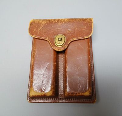 un vieil étui en cuir marron à deux compartiments posé sur une surface blanche