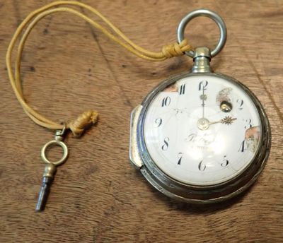 a silver pocket watch and a key on a wooden table