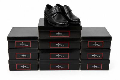 six boîtes noires sur lesquelles sont posées des chaussures noires, le tout posé sur une surface blanche