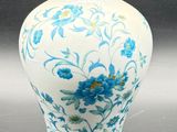 a white vase with blue flowers on it on a table