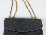 une image représentant un sac à main noir auquel est suspendue une chaîne